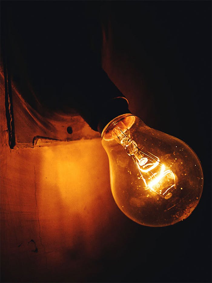 A close-up view of an illuminated incandescent light bulb glowing warmly against a dark background.